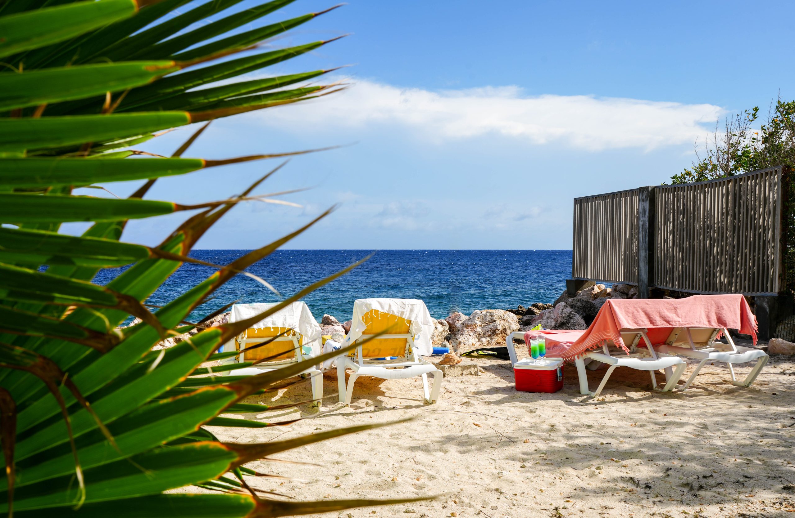 Sun loungers and palm leaves on a sandy beach overlooking the Caribbean Sea – Dushi Pietermaai Apartments