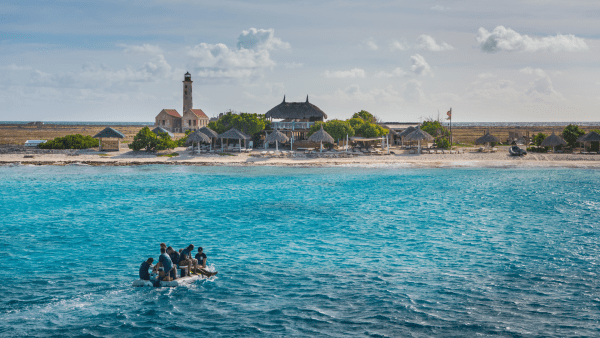 View of Klein Curaçao with lighthouse, huts and boat approaching shore