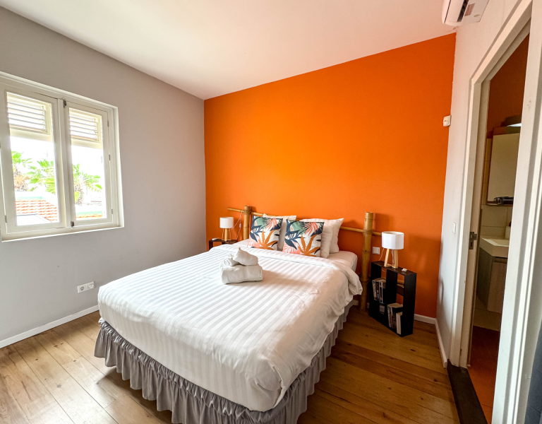 Apartment Soleil bedroom with orange wall and wooden floor.