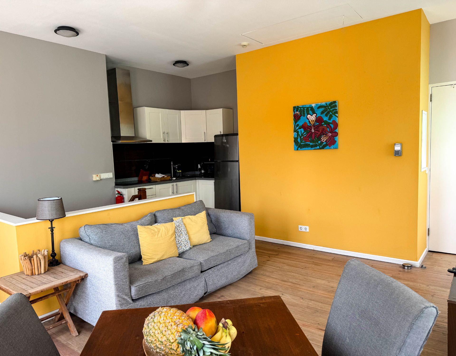 Bright living room with yellow accent wall and modern kitchen – Tierra apartment Curaçao