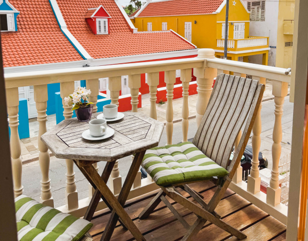 Private balcony with tropical wooden chairs overlooking colourful street – Tierra apartment