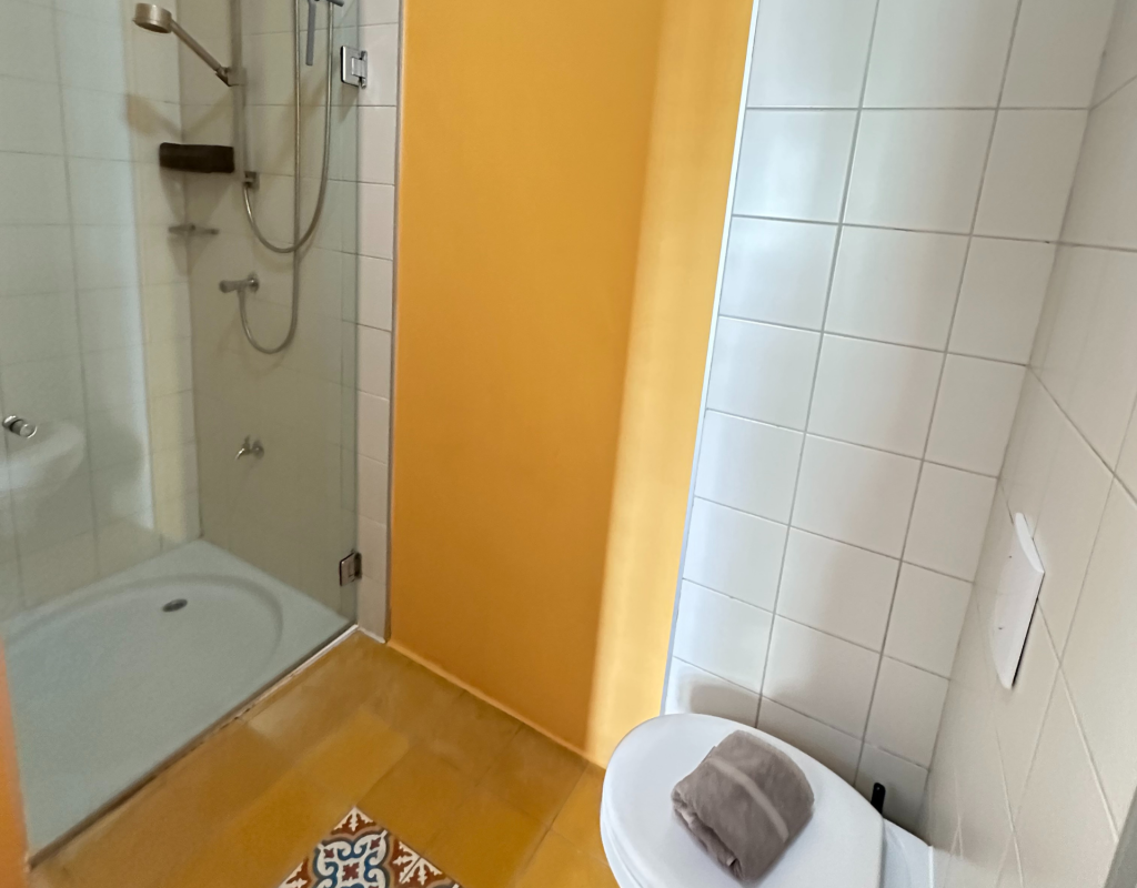Bathroom with shower, white tiles and yellow floor – Tierra apartment Curaçao