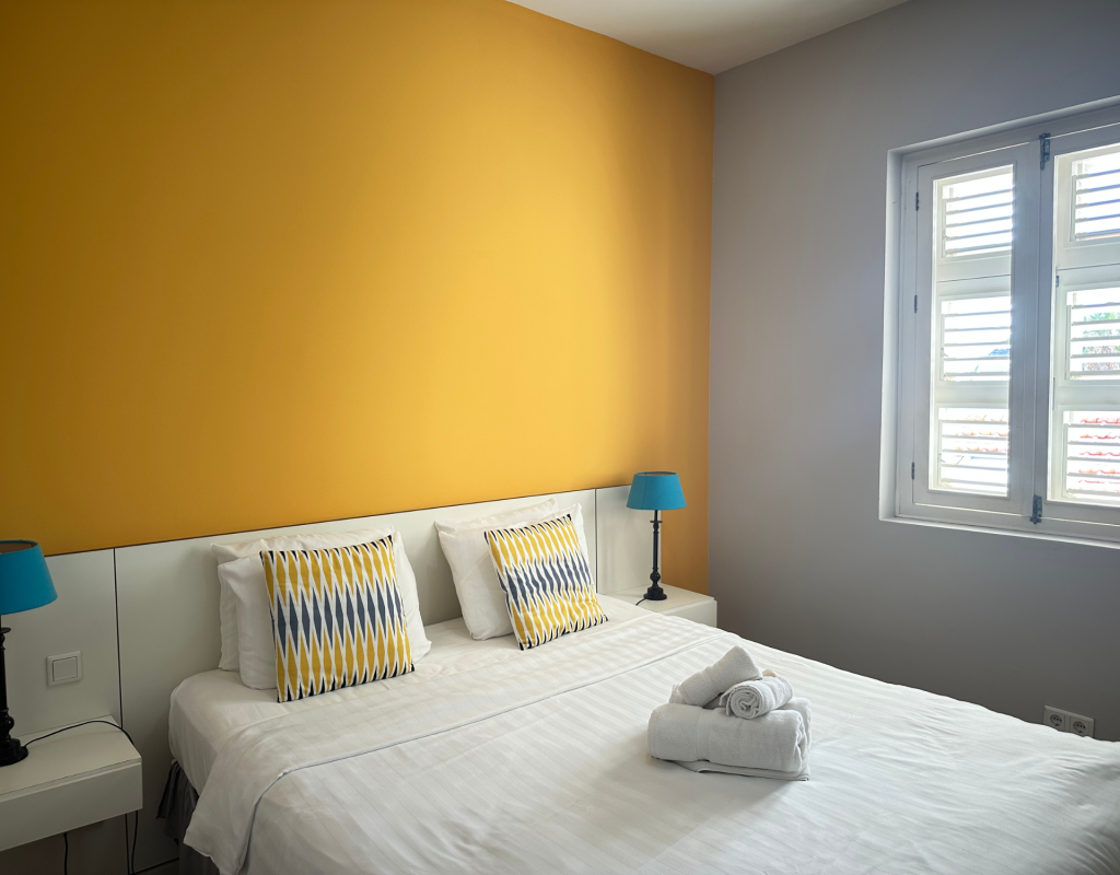 Bedroom with yellow accent wall and two windows – Tierra apartment
