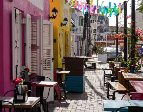 Colourful street in Pietermaai with pink and yellow facades, outdoor cafés and hanging flags – Curaçao