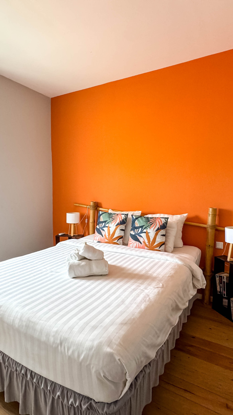 Tropical-style bedroom with orange accent wall at Dushi Pietermaai Apartments, Curaçao