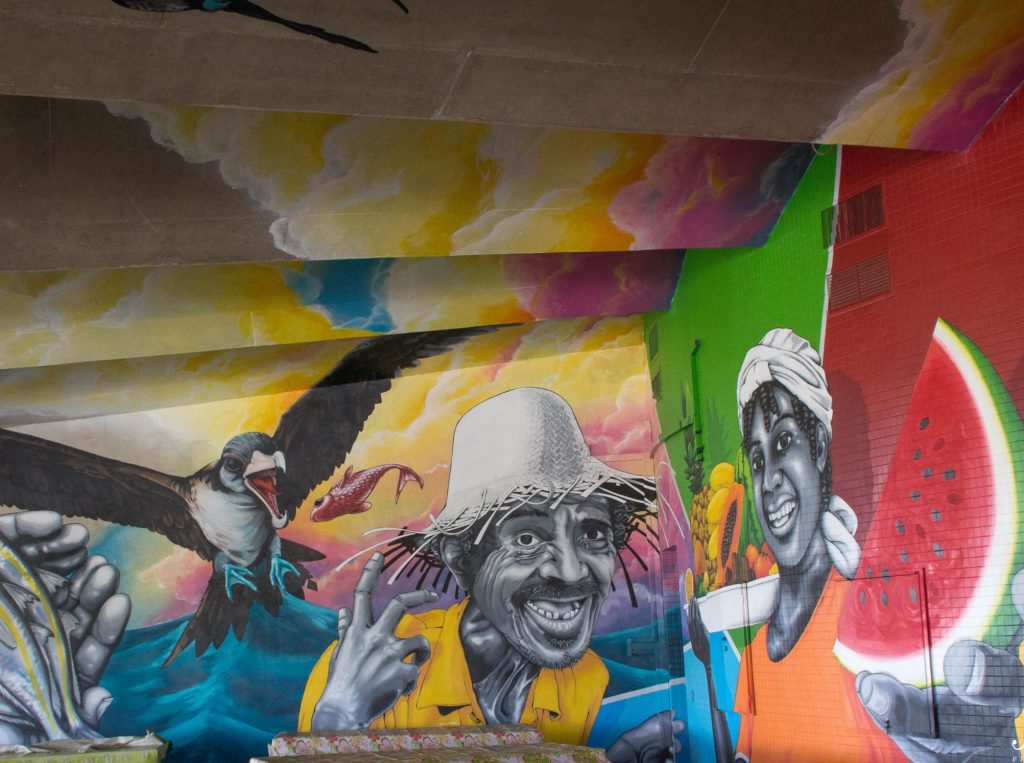 Colourful street art mural in Curaçao featuring smiling locals, tropical birds, and bold island colours